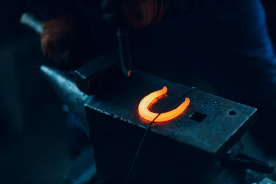 Blacksmith forges and making metal horseshoe with hammer and anvil at forge.