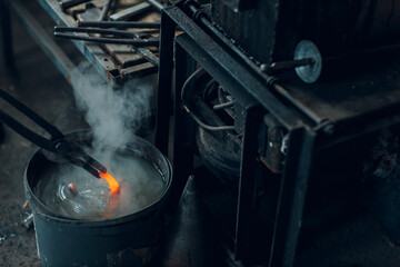 Blacksmith forges and tempering metal horseshoe in jar with water at forge.