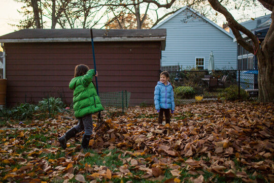 a happy boy and girl rake a pile of leaves at sunset
