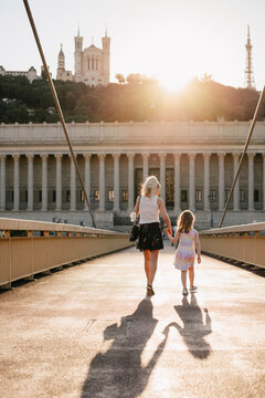 Rear view of mother with daughter walking on Palais-de-Justice footbridge against sky during sunset