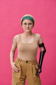 Portrait of young girl with prosthetic arm looking at camera standing against pink background