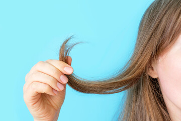 Girl holding her hair with split ends close-up on blue background.