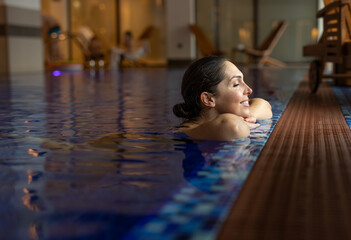 A beautiful young woman is enjoying a massage in a SPA center swimming in the indoor pool