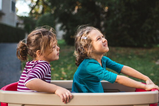 two cute little girls sit happily together in a wagon