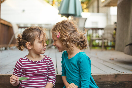 two happy little girls sit close together outside, talking