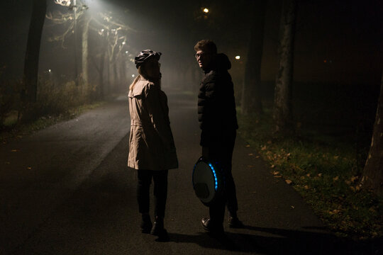 Couple with an electric unicycle looking at the camera at night time