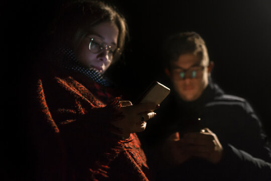 Young Couple Looking At Phones Outside At Late Evening