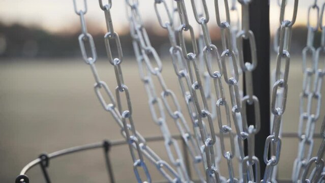 Blue Inner Core Disc Golf Disc Hits Chains of Disc Golf Basket and are then Picked Up By Hand of Disc Golfer (Close Up and Slow Motion)
