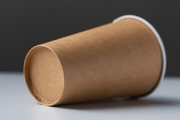 Disposable cardboard biodegradable glass on a white table, gray background.