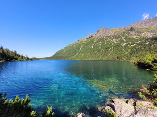 A beautiful panorama of the landscape - mountains and a mountain lake, in the smooth surface of which a cloudless sky is reflected on a sunny day