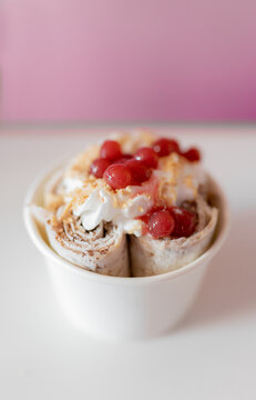 Close up of a rolled ice cream decorated with strawberry bubbles and nut toppings