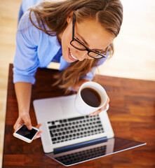 Looking forward to a day of rest and relaxation. High angle shot of a young woman having coffee while sitting with her laptop and cellphone.