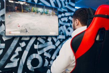 Young man plays on game console with gamepad sitting on chair.