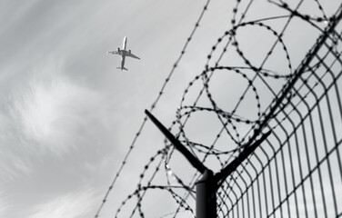 Airplane silhouette in the background. Barbed wire fence detail. Black and white.
