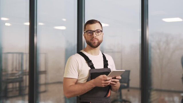 Portrait of an adult man in a work uniform with a translation tablet looking at the camera and smiling at it