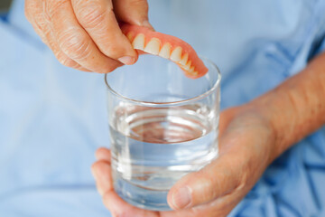 Asian senior woman patient clean teeth denture in a glass with solution for chew food.