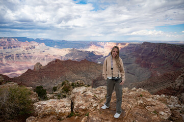 Fototapeta premium Portrait of a smiling young blonde girl with a vintage photo camera on the precipice of the Grand Canyon