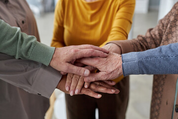 Close up of senior people stacking hands during support group session in retirement home