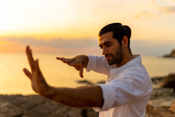 Caucasian man martial art practice and meditation with ocean nature on rocky coastal hill at summer...
