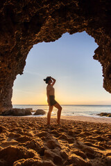 a woman standing at Tegal Wangi Beach, Jimbaran, Bali taken from inside the cave. Girl standing outside the cave on the beach while sunset.