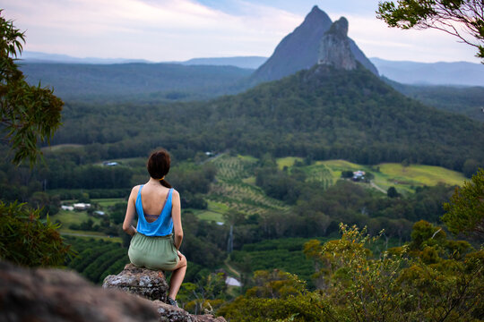 Beautiful girl sits on top of the Ngungun Mountain and admires the Beerwah and Coonowrin mountains in Glass House National Park, Queensland, Australia