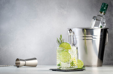Gin tonic classic cocktail drink with dry gin, bitter tonic, lime and ice. Gray table background