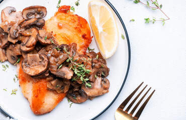 Fried chicken fillet with mushrooms and onion in white wine sauce with thyme on plate, white background, top view