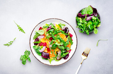 Beet and orange healthy salad with arugula, lamb lettuce, red onion, walnut and tangerine, gray kitchen table. Fresh useful vegan dish for healthy eating - obrazy, fototapety, plakaty