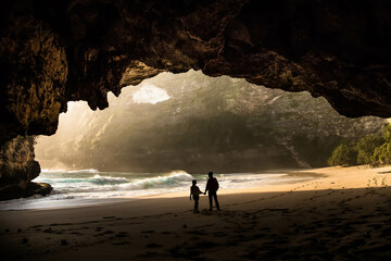 
Silhouette photo of a couple at Kelingking Beach, Nusa Penida, Bali taken from inside the cave. People are outside the cave on the beach. - obrazy, fototapety, plakaty