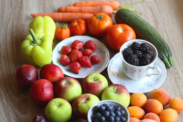 Berries in vintage porcelain dishes, other healthy fruit and vegetable on wooden table. Selective focus.