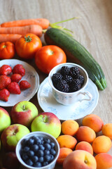 Berries in vintage porcelain dishes, other healthy fruit and vegetable on wooden table. Selective focus.