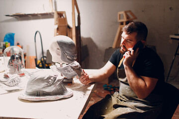 Artisan craftsman with mobile cell phone create mask based on plaster cast. Gypsum mold and plastic mask sculpting.