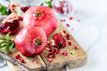 Red ripe pommegranates on a wooden cutting board with split open fruit pieces and juicy seeds