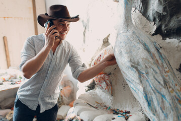Man mosaics master in hat canadian with mobile cell phone at smalt glass mosaic panel. Male mosaicist at work