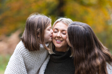 Two happy girls daughters kissing their mother in the cheeks