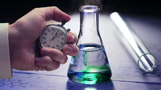 Chemical tubes, reaction formulas and stopwatch in a hand