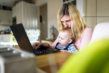 Woman and baby boy looking at computer at home - 578980437