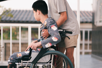 Young man with disability on wheelchair and father or volunteer or caregiver at happy time in the house, Caring for love and positive energy from parents, mental health, Family Caregiving concept.