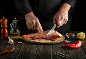 Professional chef prepares Sebastes fish. Preparing to cook fish food. The cook cuts with knife a red fish before roast