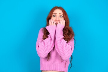 Anxiety - young woman wearing pink sweater over blue background covering his mouth with hands...