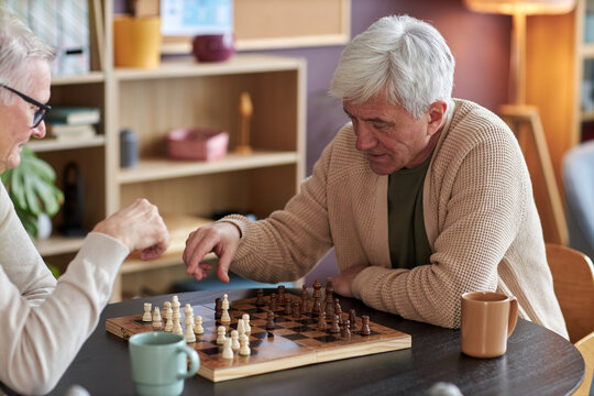 Portrait of white haired senior man playing chess at table in retirement home