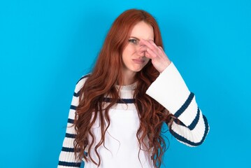 young caucasian woman wearing overalls over blue background , holding his nose because of a bad...