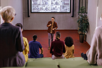 Businessman giving a speech, standing in the conference hall, using a projection screen.