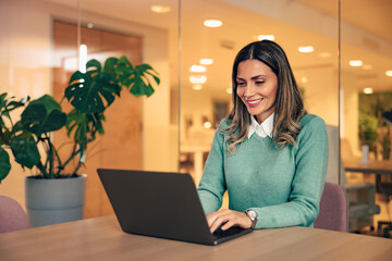 Smiling businesswoman chatting online with clients over the laptop, indoors.