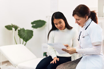 A careful female doctor holding the blood results of a female Asian patient.