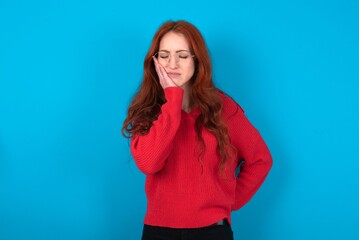 young woman wearing red sweater over blue background with toothache