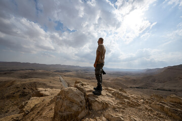 Fototapeta premium A man is standing on the edge of a cliff and looking down at the valley in rhe Negev desert in Israel.