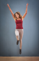On tope of the world. a happy young woman jumping in the air against a gray background.