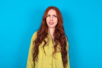 young woman wearing green sweater over blue background sticking tongue out happy with funny...