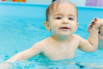 Fototapeta na wymiar A 2-year-old little boy learns to swim in a pool with a coach. Swimming lessons for children